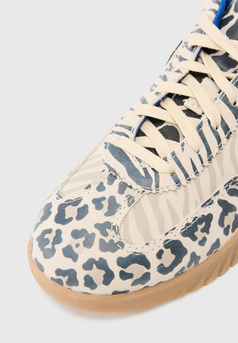 Zapatillas beige con un patrón de leopardo azul, tela texturizada, punta redondeada y suela de goma con diseño de cordones.