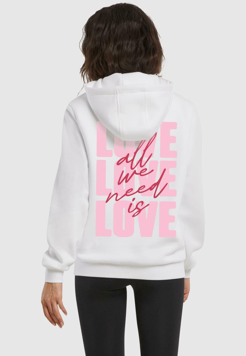 Sudadera blanca con un diseño casual y textura suave, que presenta un atrevido texto gráfico en color rosa en la parte trasera que dice "todo lo que necesitamos es AMOR".