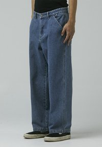 Wide-leg blue denim jeans with a faded wash, featuring a front button and zip closure. Straight-cut silhouette with side pockets.