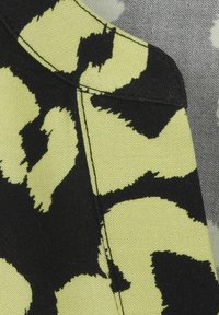 Stoff mit einem schwarz und neongelben Leopardenmuster, der eine strukturierte Oberfläche und kontrastierende Nähte aufweist.