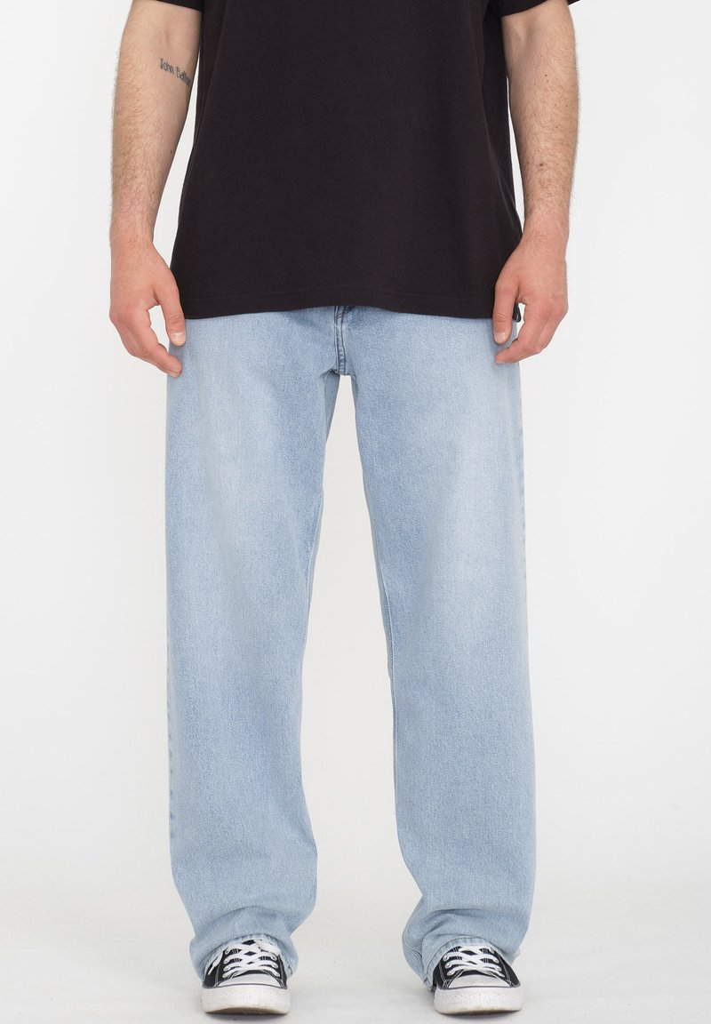 Jeans de mezclilla azul claro con un corte suelto, diseño de pierna recta y costuras visibles, combinados con zapatillas negras.
