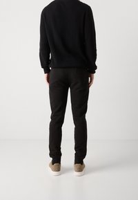 Suéter negro de canalé y pantalones negros, combinados con zapatillas de deporte beige. El suéter tiene un cuello redondo y un ajuste holgado; los pantalones son ajustados y cuentan con un bolsillo trasero.