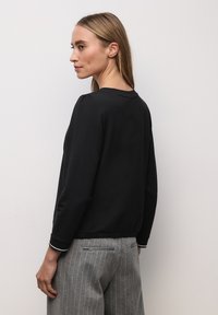 Czarna bluzka z długim rękawem, okrągłym dekoltem i marszczonymi ramionami, zestawiona z szarymi spodniami w paski, posiadającymi tylne kieszenie i dopasowany krój.