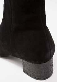 Schwarze Wildleder-Ankle-Boots mit einer runden Form und einem strukturierten Blockabsatz in einer gesprenkelten schwarzen Ausführung. Glatte Oberseite mit nahtlosem Design.