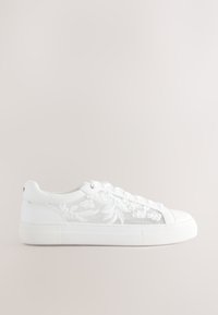 Zapatilla blanca baja con bordado floral en el lateral, cierre de cordones en el frente y suela gruesa de goma sobre un fondo neutro.