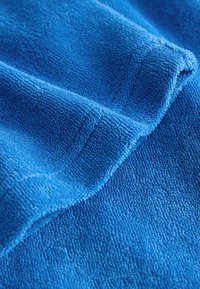 Cârpa albastră din microfibră cu bucle vizibile și o pliură, evidențiind textura moale și absorbantă pentru curățarea sau uscarea suprafețelor.