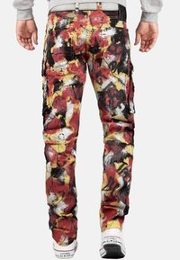Un pantalon cargo présentant un motif abstrait multicolore en rouge, jaune et noir, avec plusieurs poches et une coupe fuselée.