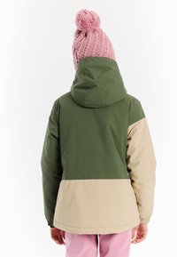 Farbblockierte Jacke mit grünen und beigen Abschnitten, Kapuze und elastischen Bündchen. Getragen mit einer rosa gestrickten Mütze, von hinten gesehen.