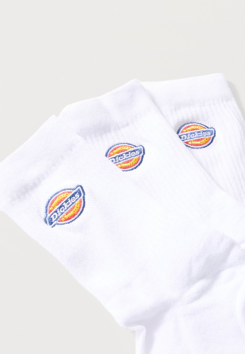 Three white crew socks with embroidered circular Dickies logos in orange, yellow, and blue near the top cuff.