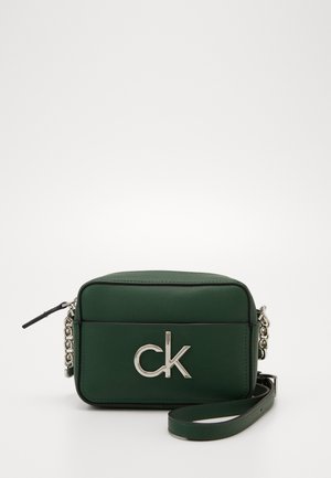 Ciemnozielona, prostokątna torebka na pasku z naturalnej skóry, z srebrnym logo "ck", łańcuchowym i skórzanym paskiem oraz zamkiem błyskawicznym na górze.