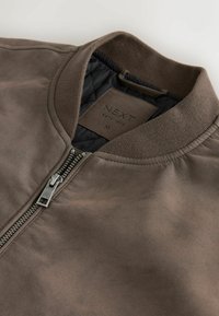 Veste bomber en daim marron avec col côtelé, fermeture éclair argentée et doublure intérieure matelassée noire, taille moyenne de la marque NEXT.