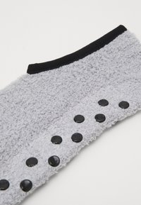 Pelēka teksturēta auduma virsma ar mīkstu, pūkainu faktūru, ar melnu apdari un sešām dekoratīvām melnām pogām gar vienu malu.