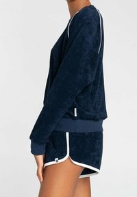 Granatowy welurowy sweatshirt z białym wykończeniem, długimi rękawami i ściągaczami, zestawiony z dopasowanymi szortami z bocznym wykończeniem i detalami marki.