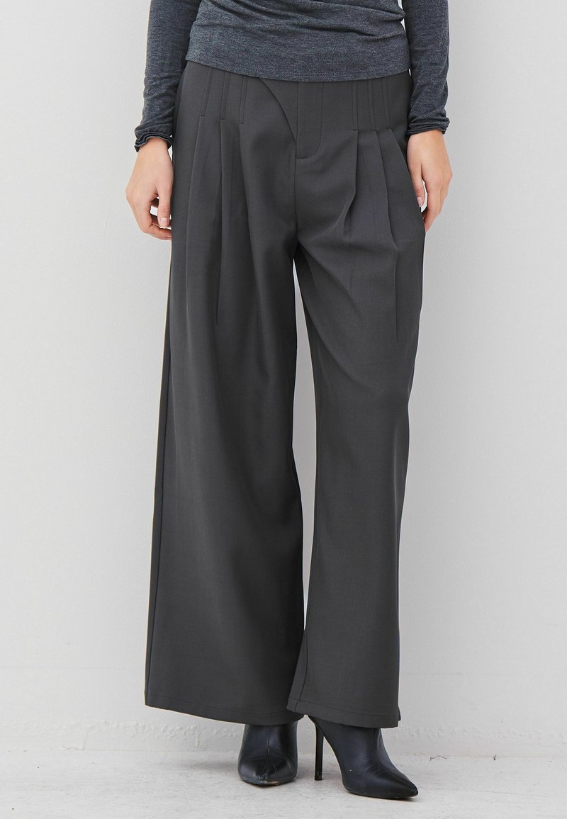 Person wearing wide-leg dark gray pants, black high-heeled ankle boots, and a fitted long-sleeve gray top against a white background.