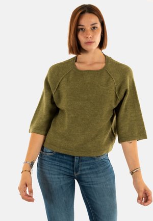 Pull court olive, à manches courtes, avec un large col et une coupe décontractée, fabriqué à partir d'un matériau tricoté doux et texturé. Associé à un jean bleu.