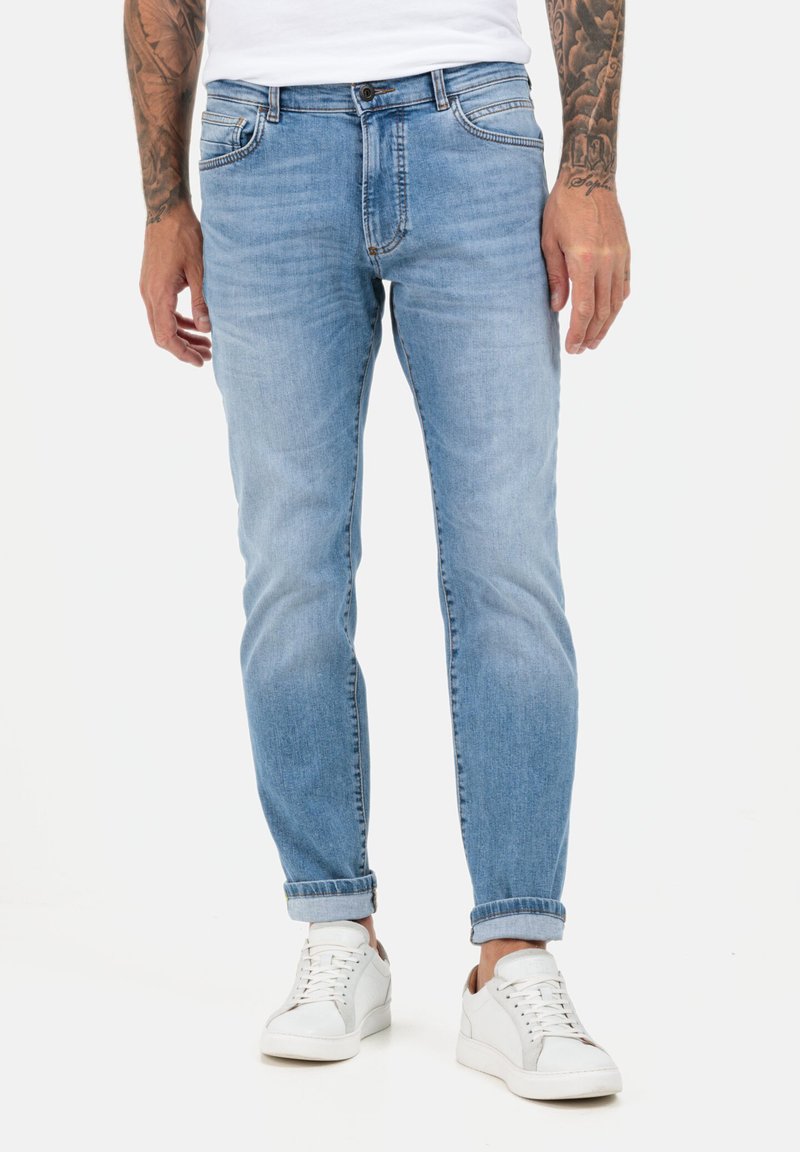 Jasnoniebieskie dżinsy w slim fit, z pięcioma kieszeniami, delikatnym efektami przetarć i podwiniętymi mankietami, w połączeniu z białymi trampkami.