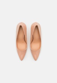 Nude kiilakorkoiset patenttinatekstiilit, joissa on terävä kärki ja sileä pinta, matalalla vampilla ja minimalistisella tyylillä.