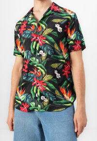 Chemise noire à manches courtes arborant un motif floral tropical vibrant en rouge, blanc et vert. Boutons sur le devant et col de style campagnard.