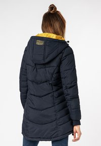 Námořnický puffer kabát s žlutým podšívkou kapuce, prošívaná textura, nastavitelná kapuce a postranní kapsy. Obsahuje štítek na zadní straně.