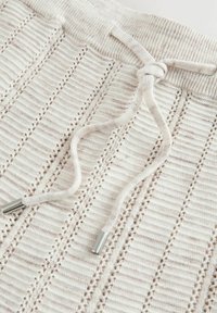 Tissu en maille avec des motifs verticaux en dentelle et un cordon de serrage noué, terminé par des embouts métalliques.