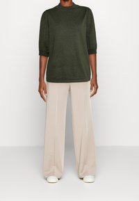 Un haut en tricot vert foncé avec un col haut et des manches bouffantes, associé à un pantalon beige à jambes larges et des baskets blanches.