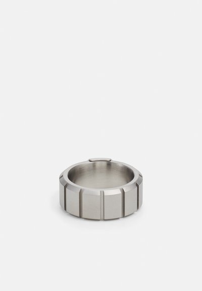 Sølv ring med en tekstureret, ribbet overflade. Fremstillet af metal, med en glat inderside og geometriske designelementer rundt om yderkanten.