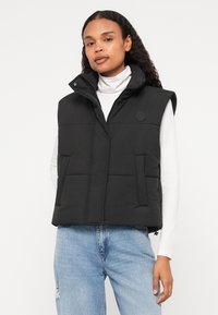 Μαύρο γιλέκο φουσκωτό με ψηλό λαιμό, κλείσιμο με φερμουάρ και μπροστινές τσέπες. Κατασκευασμένο από υλικό με επένδυση, με κυκλικό λογότυπο στο στήθος.