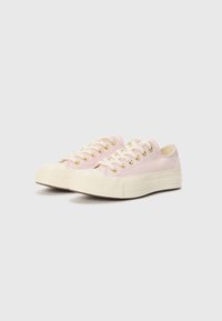 Low-top sneakers in soft pink canvas with cream accents, featuring gold eyelets, round toe, and textured white rubber sole.