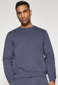 Σκούρο μπλε φούτερ από μαλακό βαμβάκι με μακριά μανίκια, στρογγυλή λαιμόκοψη και ριμπ μανσέτες. Διαθέτει μια μικρή ετικέτα λογότυπου στο στρίφωμα.