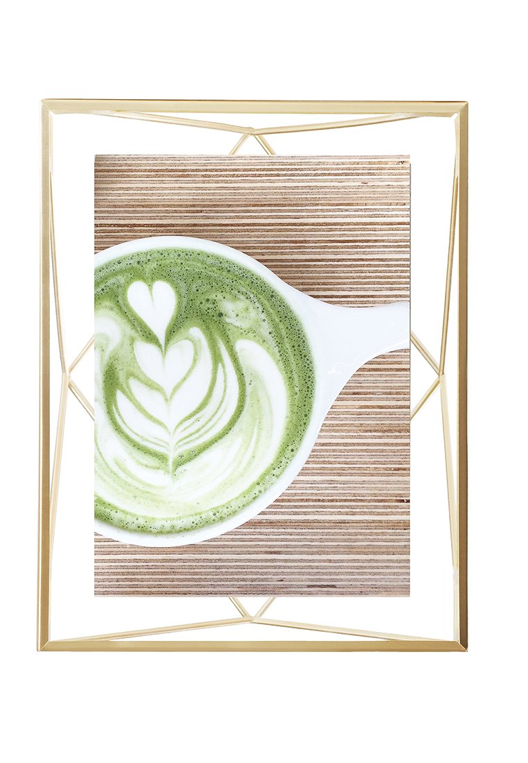 Un latte au matcha avec une mousse blanche ornée de motifs en forme de cœurs et de feuilles, servi dans une tasse blanche sur une surface en bois clair, entouré d'un cadre géométrique doré.