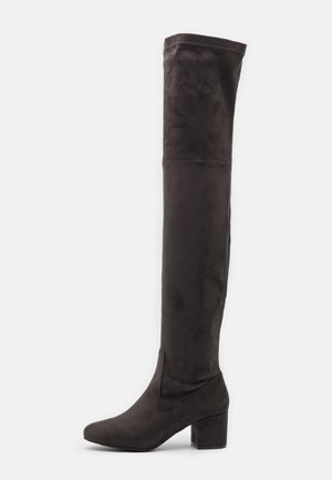 Bottes noires en suède au-dessus du genou avec un talon bloc, présentant une texture lisse et un design élégant et ajusté s'étendant jusqu'à la cuisse.