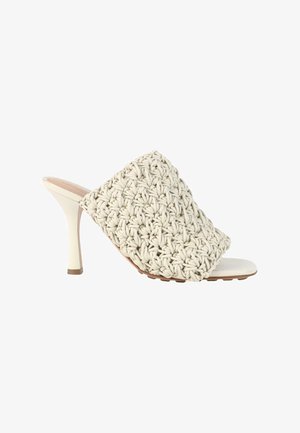 Mule beige à talon haut avec une large bride tissée et un talon fin et effilé sur fond blanc.