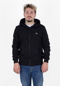 Sudadera negra con cremallera fabricada en una mezcla de algodón, con un bolsillo canguro, capucha con cordón y un pequeño logo bordado en el lado izquierdo del pecho.