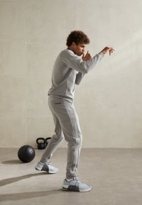 Light gray athletic sweatshirt and joggers with a textured finish, featuring side stripes, and gray sneakers in a fitness setting.