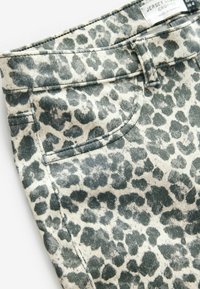 Afgeknotte jersey broek in een beige stof met een groen luipaardprintpatroon. Kenmerken zijn een platte tailleband en zijzakken.