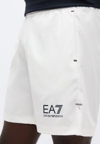Λευκά αθλητικά σορτς κατασκευασμένα από ελαφρύ ύφασμα, με ελαστική μέση και μαύρο λογότυπο EA7. Περιλαμβάνει διακριτικές πλαϊνές λεπτομέρειες.