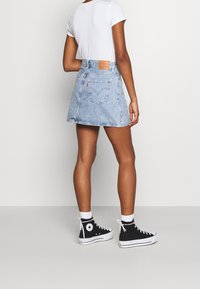 Jupe en denim mini de couleur bleu clair avec un ourlet effiloché, dotée de poches arrière et d'une étiquette de marque en cuir. Associée à des baskets montantes noires.