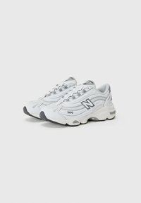 Baskets de sport blanches avec un mesh texturé et des matériaux synthétiques, présentant une accentuation grise et une semelle épaisse. Le design comprend un logo distinctif.