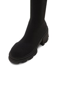 Botte noire mi-mollet avec semelle épaisse et robuste et talon bloc, matière supérieure lisse, vue de face sur fond blanc.