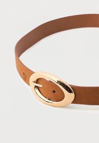 Cinturón de ante marrón con una gran hebilla ovalada dorada brillante, exhibido sobre un fondo blanco liso.