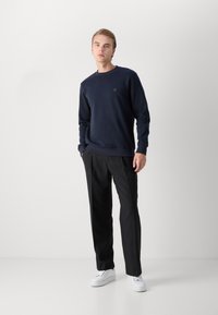 Marinblå sweatshirt med rundad halsringning och en liten logotyp, i kombination med svarta byxor och vita sneakers. Slät textur, skräddarsydd passform.