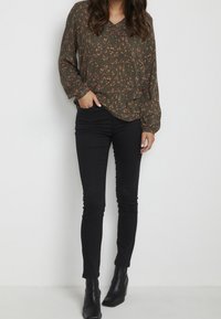 Blouse à manches longues à motif floral vert, associée à un jean skinny noir et des bottines noires ; présente un décolleté en V et une coupe décontractée.