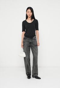 Top negro de escote redondo combinado con unos jeans grises de pierna ancha y de cintura alta. Sosteniendo un bolso blanco fruncido. Zapatos negros de punta.