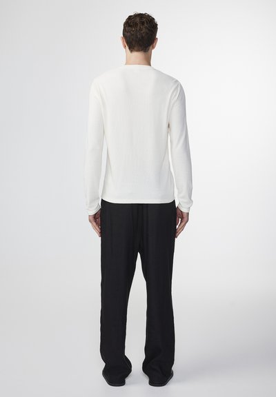 Long-sleeve white knit top with a round neckline, paired with black, loose-fitting trousers. Smooth texture with simple design details.