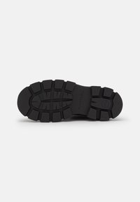 Semelle de chaussure en caoutchouc noir avec un motif de semelle profond. Elle présente une forme arrondie et une texture durable, marquée avec des détails de marque et de taille.