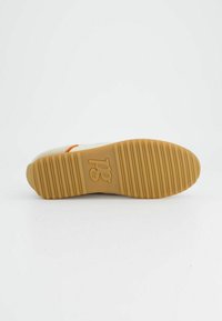 Semelle d'une basket avec un fond en caoutchouc texturé comportant des rainures horizontales et verticales, de couleur beige, avec un détail de marque au centre.