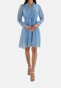 Robe chemise bleu clair en tissu semi-transparent, avec des manches longues, un devant à boutons et une taille cintrée.