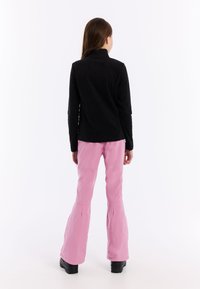 Zwarte langemouwen top, roze flared broek en zwarte laarzen. De outfit heeft een soepele textuur en een getailleerd silhouet.