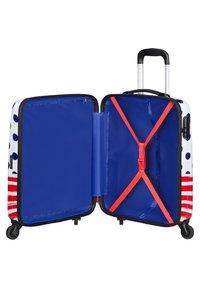 Valise rigide avec intérieur bleu, extérieur blanc orné de pois bleus et de rayures rouges, sangles croisées intérieures et roues pour la mobilité.