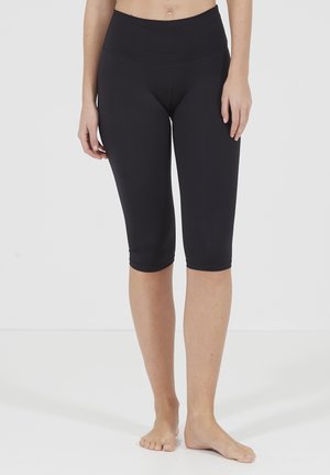 Schwarze Capri-Leggings aus dehnbarem Material mit hohem Bund und glatter Textur, die knapp unter dem Knie enden.